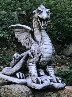 a statue of a dragon sitting on top of a rock in front of some bushes