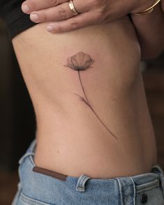 a woman's stomach with a single flower tattoo on her left side ribcage