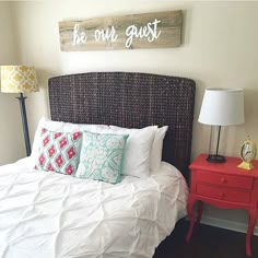 a bed with white sheets and pillows in a bedroom next to a red night stand