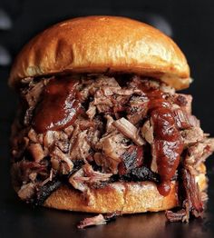 a pulled pork sandwich with bbq sauce on a black surface, ready to be eaten