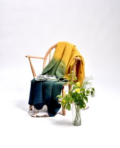 a wooden chair sitting next to a vase with flowers in it and a blanket on top of the chair