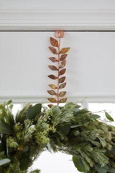 two wreaths are hanging on the window sill with greenery in front of them