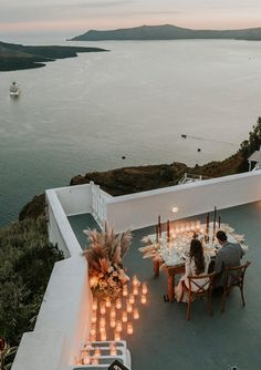 two people sitting at a table with candles in front of them on top of a roof