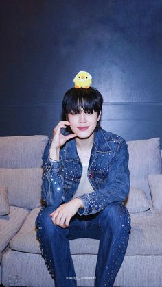 a woman sitting on top of a couch wearing a jean jacket and a rubber ducky hat