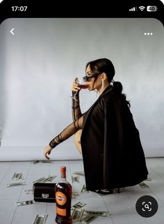 a woman is sitting on the floor with money falling around her and drinking from a bottle