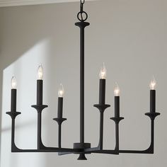 a black chandelier with six lit candles hanging from it's center rod