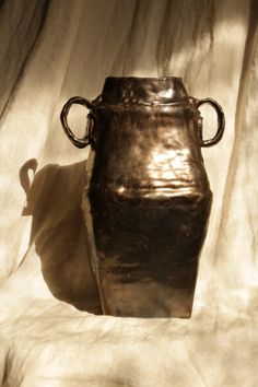 a large metal vase sitting on top of a white sheet