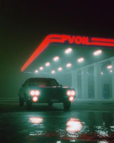 a car is parked in front of a gas station with neon lights on the side