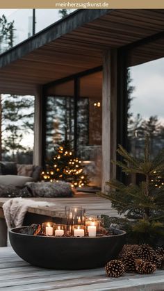 candles are lit on a table outside in front of a house with christmas trees and pine cones