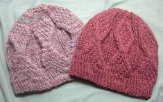 two knitted hats sitting on top of a bed next to each other in different colors