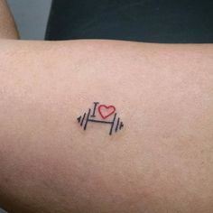 a small tattoo on the arm of a person with a red heart and barbell