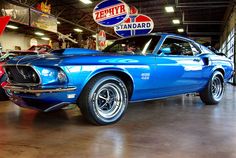 an old blue mustang car is parked in a garage with other cars and signs on the wall