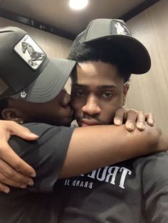 two men hugging each other in a locker room with baseball caps on their heads and arms