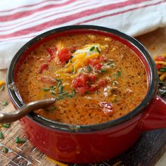 a red pot filled with soup on top of a wooden cutting board