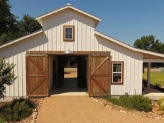 a white barn with wooden doors and gravel path leading to the front door, on a sunny day