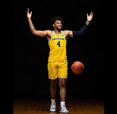 a man in a yellow uniform is holding his hands up and standing next to a basketball