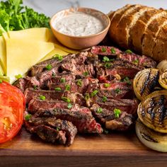 steak, onions, bread and vegetables on a cutting board