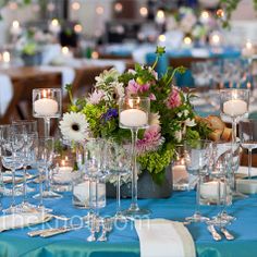 a centerpiece with candles and flowers on a blue table cloth at a wedding reception