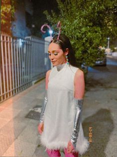 a woman in white dress and pink boots standing on sidewalk next to fenced area