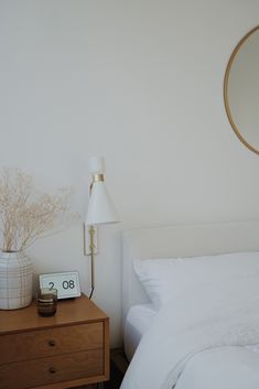 a bed with white sheets and pillows next to a nightstand with a clock on it