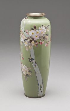 a green vase with white flowers painted on the front and bottom, sitting on a gray surface