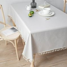 a white table cloth with tassels on it and two cups, saucers and an avocado