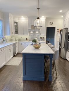 a large kitchen with white cabinets and blue island in the center is lit by two pendant lights