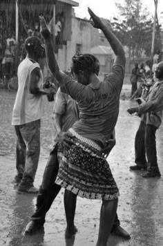 people are dancing in the rain with umbrellas and other people standing around watching them