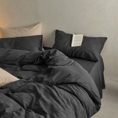 an unmade bed with black sheets and pillows