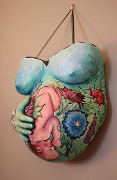 a ceramic sculpture of a woman with flowers on her body hanging from a hook in a room