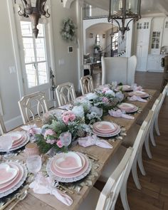 a dining room table set with pink plates and flowers on the placemats for dinner