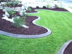 a garden with grass and rocks in the middle, along side a sidewalk that is lined with mulch