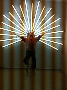 a man sitting on a stool in front of a wall with lights coming from it