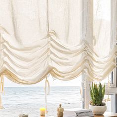 a living room with a window covered in sheer curtains and a potted plant on the table