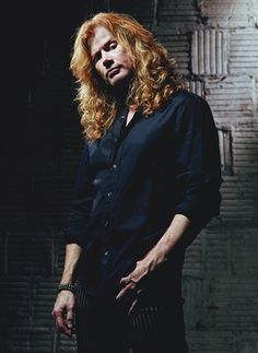 a man with long red hair standing in front of a brick wall and looking at the camera