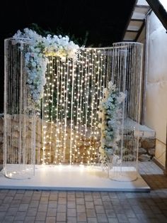 a white wedding arch decorated with flowers and lights for the entrance to the ceremony room