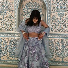 a woman standing in front of a wall wearing a blue and silver outfit with her hands on her hips