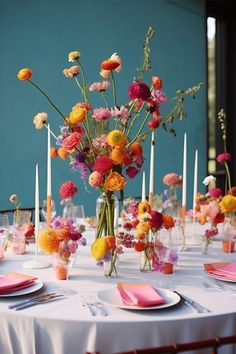 an arrangement of flowers and candles on a table with plates, napkins and place settings