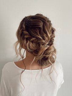 a woman with her hair in a low braid up to the side, wearing a white t - shirt