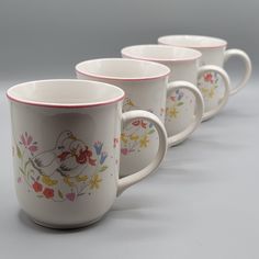 four coffee mugs are lined up in a row on a gray surface with flowers and birds painted on them