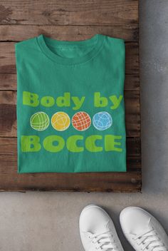 "Introducing our \"Body by Bocce\" T-shirt, a must-have for all bocce enthusiasts! This stylish and comfortable tee is perfect for showcasing your love for the popular Italian lawn game. Crafted with the finest quality materials, this shirt offers a flattering fit that will highlight your love for both fashion and bocce. Whether you're enjoying a friendly game at the park or simply relaxing with friends, this \"Body by Bocce\" T-shirt is the perfect addition to your wardrobe. Get ready to make a statement and show off your bocce skills with this unique and eye-catching tee!  You'll be the talk of the Bocce Court. .: 100% ring-spun cotton (fiber content may vary for different colors) .: Light fabric (4.5 oz/yd² (153 g/m .: Eurofit .: Tear-away label .: Runs true to size" Bocce Court, Bocce Ball, Balls Shirt, Lawn Games, Team Shirt, Team Shirts, Our Body, The Park, San Jose