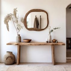 a wooden table topped with vases next to a mirror and plant on top of it