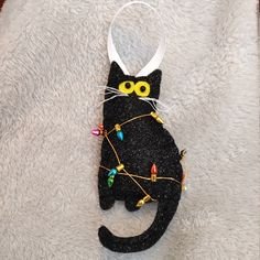 a black cat with yellow eyes is hanging on a white towel in the shape of a christmas ornament