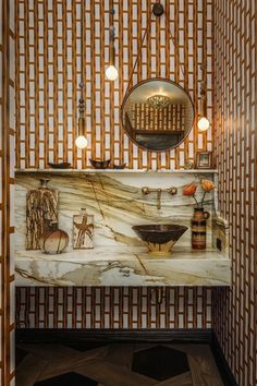 a bathroom with a marble counter top and gold wallpaper on the walls, along with an oval mirror above it