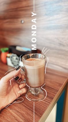 a woman holding a cup of coffee on top of a wooden table with the words monday written above it