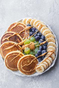 a plate with pancakes, blueberries, and bananas on it next to some fruit