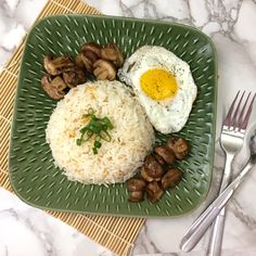 a green plate topped with rice, mushrooms and an egg on top of it next to silverware