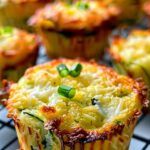 several muffins on a cooling rack with green onions and cheese in the middle