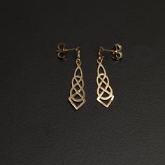 Immerse yourself in the timeless allure of these 10K gold long Celtic style drop earrings, featuring a captivating double trinity knot cutout design. The intricate craftsmanship and elegant design make these earrings a symbol of Celtic heritage and modern sophistication. The earrings, measuring 2.7 cm (1 inch) in length and 7mm (.25 inches) at the widest part, are crafted with precision and attention to detail. The flat design adds a contemporary touch, while the double trinity knot cutout creates a symbolic and visually striking element. The front of the earrings boasts a smooth surface, enhancing their sleek and polished appearance. On the back, small dots provide added texture, creating a balanced and tactile piece. The use of 10K gold ensures a lustrous and enduring finish. With posts Symbolic Bronze Drop Earrings, Ornate Dual-tone Earrings Gift, Celtic Knot Jewelry The Irish Jewelry Company, Celtic Knot Earrings, Celtic Heritage, Celtic Earrings, Trinity Knot, Celtic Style, Beaded Statement Necklace