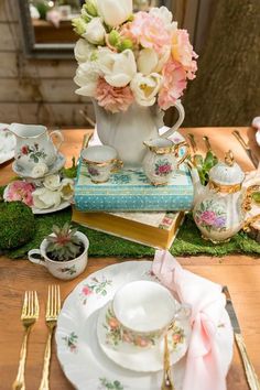 a table set with tea cups, saucers and flowers in vases on top of books